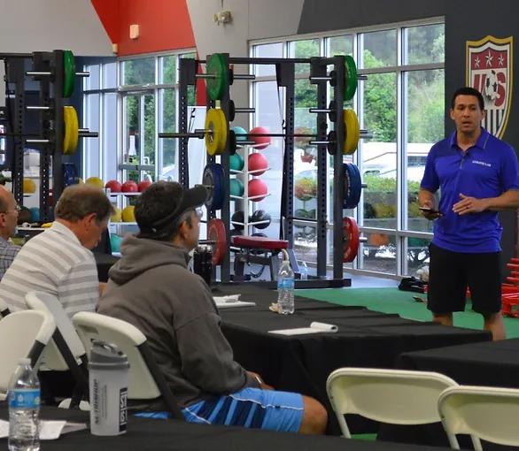 a trainer talking to a few men sitting at a table